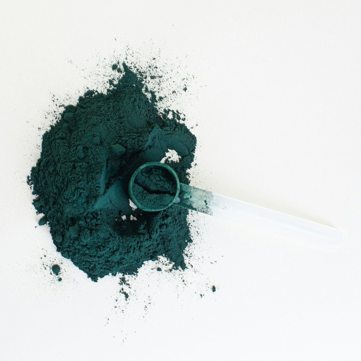 Petit tas de poudre vert-bleu et sa mesurette sur fond blanc
