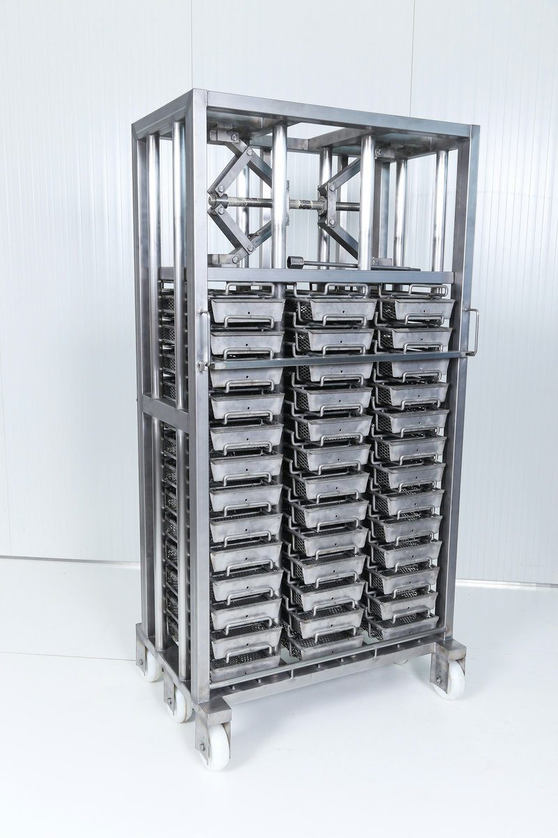 Chariot en inox chargé de plusieurs claies superposées, prêt à entrer dans un séchoir
