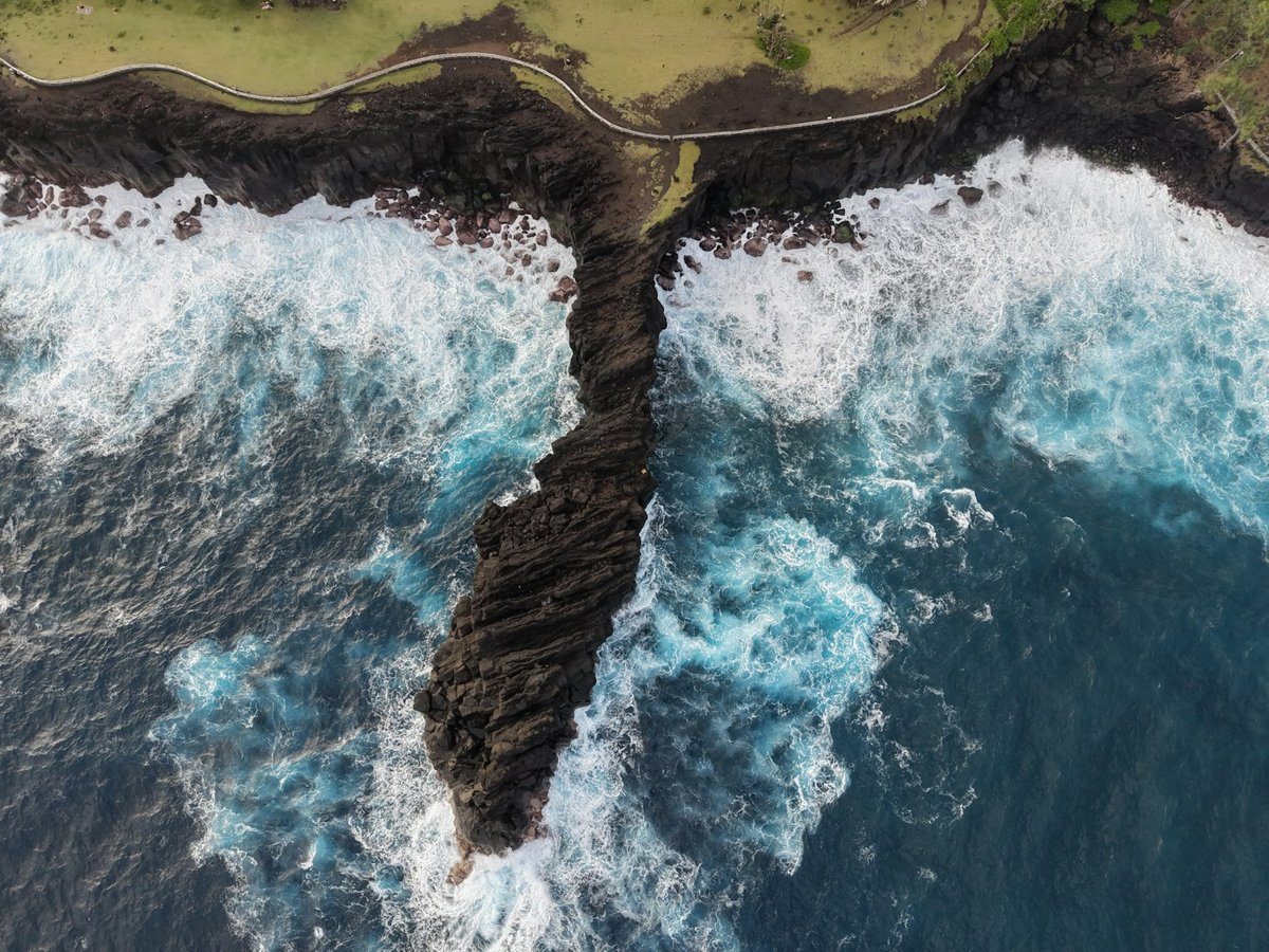 Coulée de lave noire entrant dans l'océan, battue par les vagues, vue du ciel