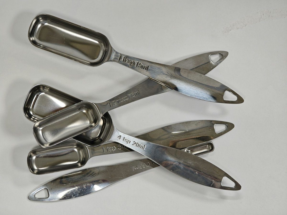 Jeu de cuillères doseuses en inox alignées sur un fond blanc